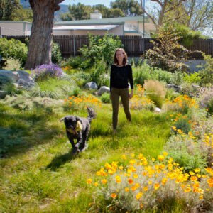 Goldn poppies and an abundance of vibrant color surround Cassy and pup Dara as they stroll through a lush meadow.